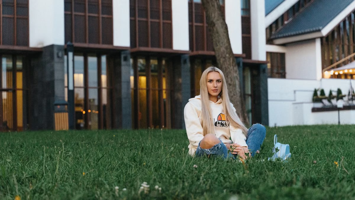 Woman sitting on grass in front of modern building in Minsk, Belarus, enjoying the serene outdoor atmosphere.